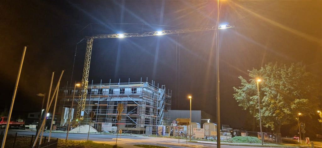 Rohbau eines Wohngebäudes am Abend, beleuchtet von Baustellenstrahlern, daneben ein Turmdrehkran